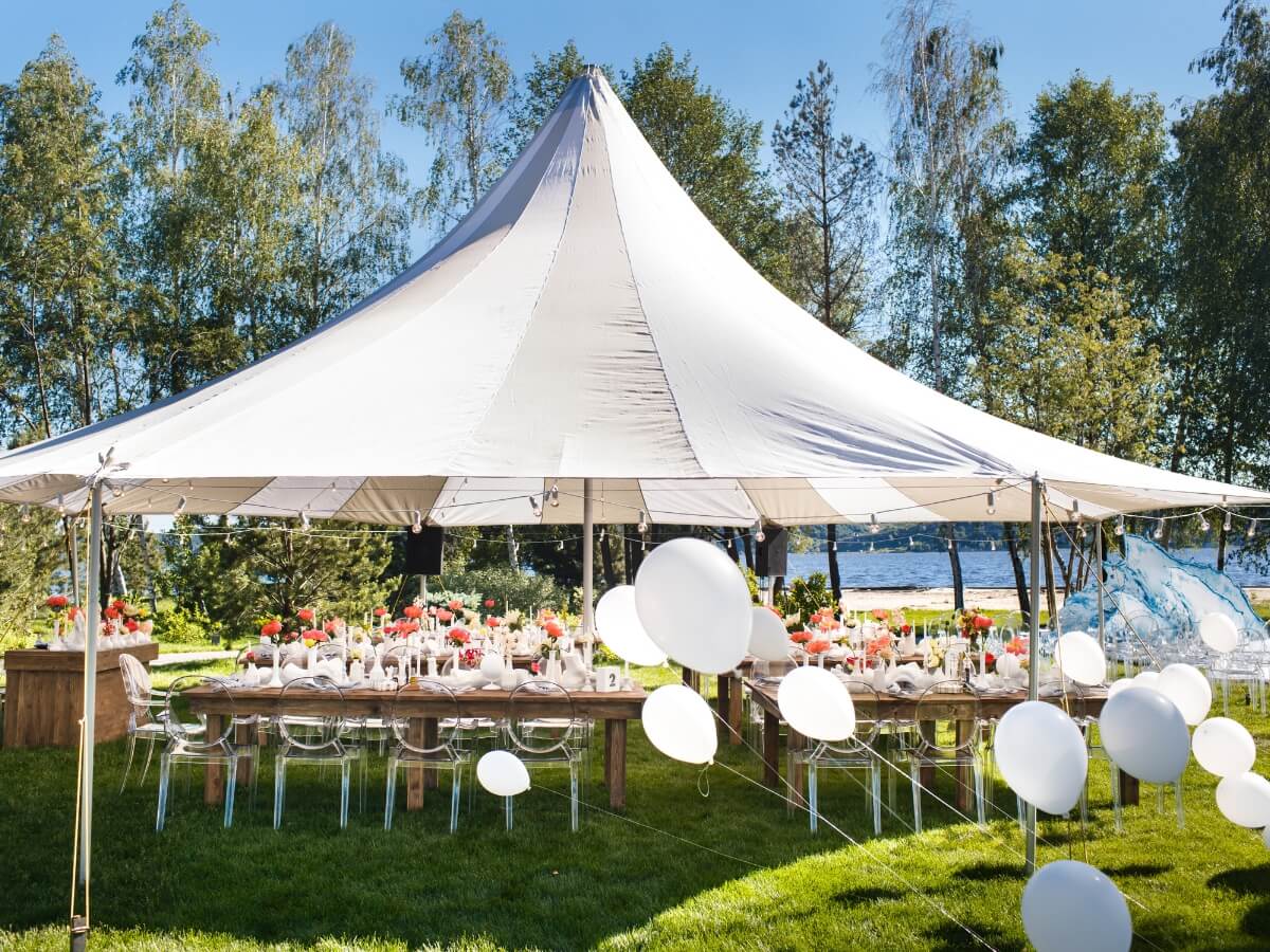 Párty stan v prírode ponad prestreté stoly, v popredí biele balóny.