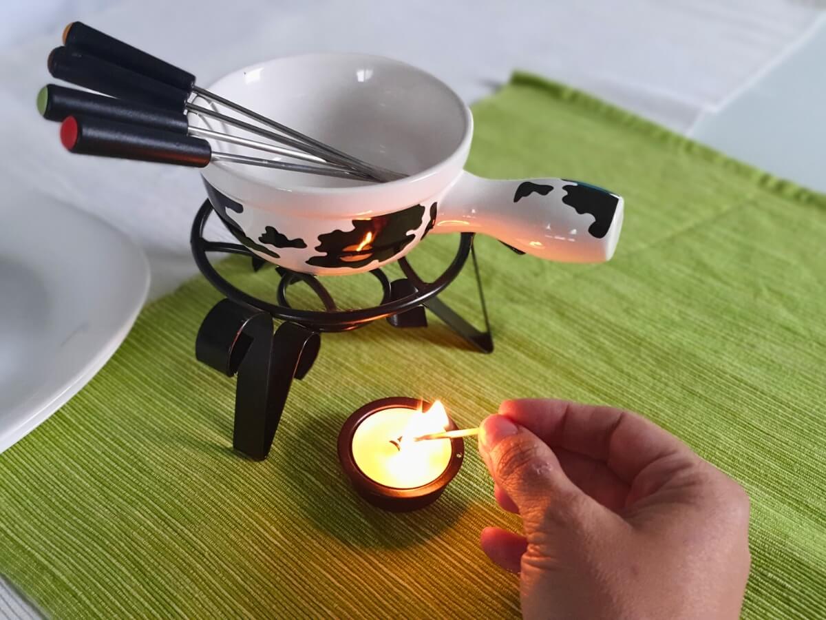 Fondue so sviečkou na zelenom prestieraní a bielom behúni.