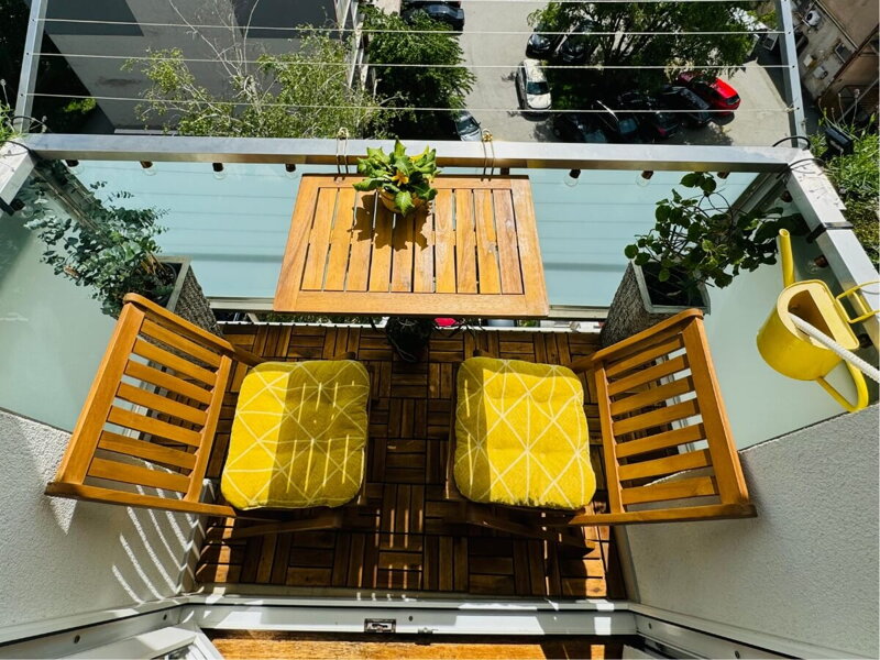 Malý balkón s dreveným sedením a žltými doplnkami.